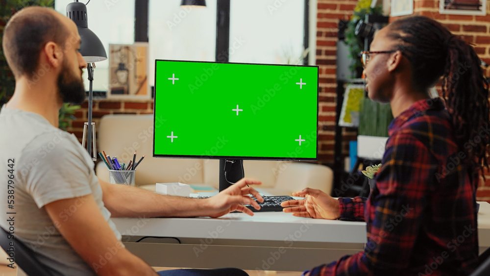 Poster diverse team working on computer with greenscreen at desk, using monitor to examine isolated display