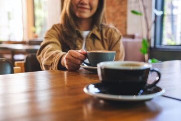 Closeup image of a young woman holding and drinking coffee with friend in cafe