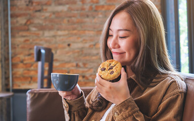 Portrait image of a young woman holding coffee cup and a piece of chocolate chip cookie