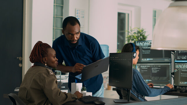 Team of software developers talking about source code running on laptop to work on artificial intelligence server development. Database admins collaborating on data programming group project.