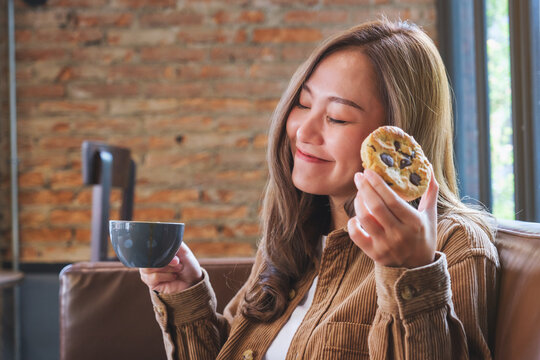 Portrait image of a young woman holding coffee cup and a piece of chocolate chip cookie