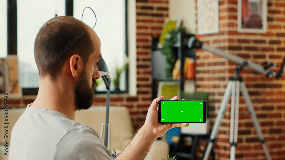 Poster male employee checking horizontal greenscreen display on mobile phone, looking at smartphone with is