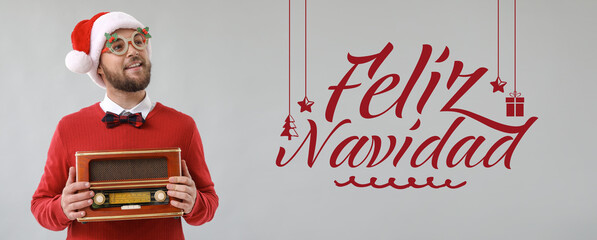 Young man in Santa hat holding retro radio receiver and text FELIZ NAVIDAD (Spanish for Merry...