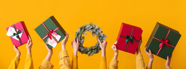 Many hands with Christmas gifts and wreath on yellow background