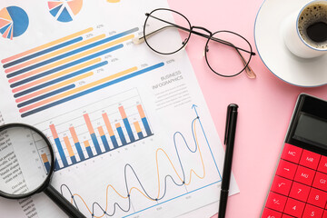 Business charts, cup of coffee and stationery on pink background