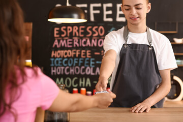 Young male barista receiving payment from visitor in cafe