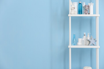 Fototapeta na wymiar Shelf unit with bath accessories for children and cute toys near blue wall