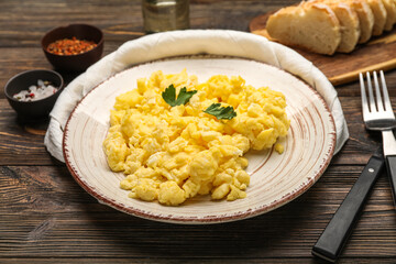 Plate of tasty scrambled eggs on wooden table, closeup