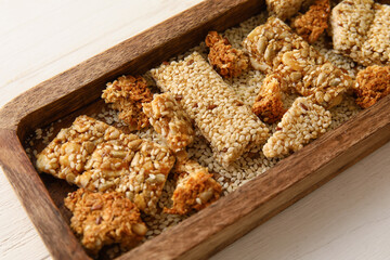 Board with pieces of tasty sesame kozinaki on light wooden background, closeup