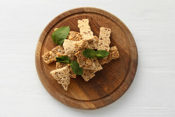 Wooden board with pieces of tasty sesame kozinaki on light wooden background