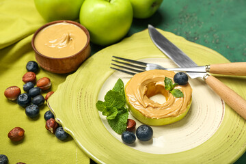 Plate of tasty apple round with nut butter, blueberry and hazelnuts on color background, closeup
