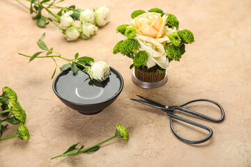 Kenzan with ikebana, bowl of water and scissors on beige background