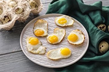 Plate with fried quail eggs on dark wooden table, closeup