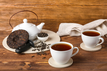 Cups of puer tea and teapot on wooden background