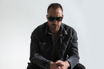 Fototapeta premium frowning man with sunglasses holding elbows on knees and sitting