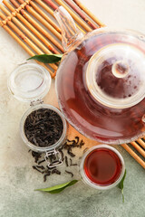 Glass cup of black tea, teapot and jar with dried leaves on light background, closeup