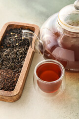 Cup of aromatic black tea, teapot and dried leaves on light background, closeup