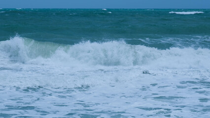 View of sea waves on the beach of tropical seas in Thailand. Strong sea waves crash to shore in the rainy season. Beautiful sea waves with foam of blue and turquoise color.