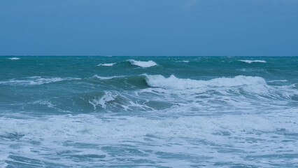 View of sea waves on the beach of tropical seas in Thailand. Strong sea waves crash to shore in the rainy season. Beautiful sea waves with foam of blue and turquoise color.