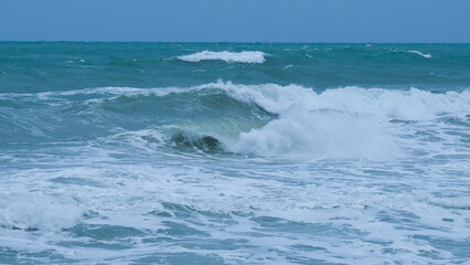 View of sea waves on the beach of tropical seas in Thailand. Strong sea waves crash to shore in the rainy season. Beautiful sea waves with foam of blue and turquoise color.