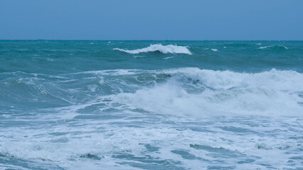 Fototapeta premium View of sea waves on the beach of tropical seas in Thailand. Strong sea waves crash to shore in the rainy season. Beautiful sea waves with foam of blue and turquoise color.