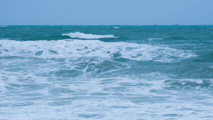 View of sea waves on the beach of tropical seas in Thailand. Strong sea waves crash to shore in the rainy season. Beautiful sea waves with foam of blue and turquoise color.