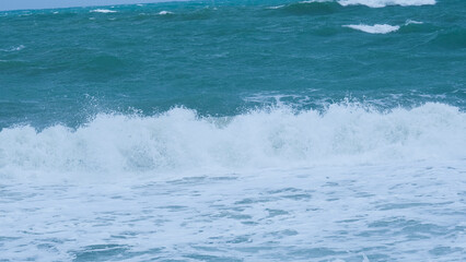 View of sea waves on the beach of tropical seas in Thailand. Strong sea waves crash to shore in the rainy season. Beautiful sea waves with foam of blue and turquoise color.