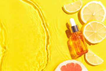 Bottle of citrus serum and fruits in water on yellow background