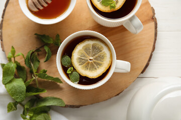 Board with cups of black tea, lemon, mint and honey on white wooden background, closeup