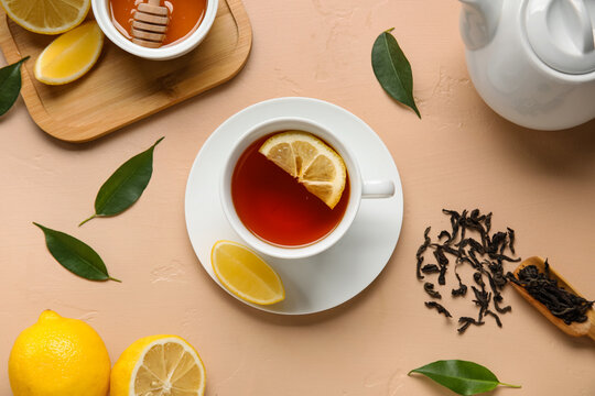 Cup of black tea with lemon and leaves on beige background