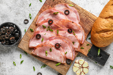 Wooden board with slices of tasty ham, black olives and bread on light background