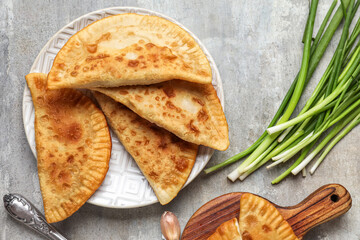 Plate with tasty chebureks and green onion on grunge background