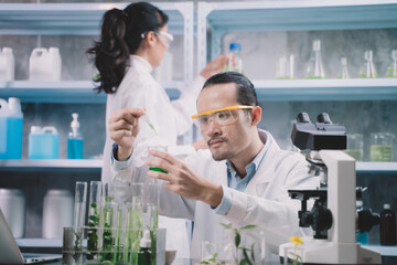 Researcher man are drop liquid to a beaker in his hand and researcher woman are picking up the...