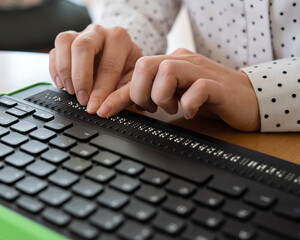 A blind woman uses a computer with a Braille display and a computer keyboard. Inclusive device.