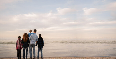 Family on sandy beach near sea, back view, standing at seaside watching the horizon. Summer vacation concept