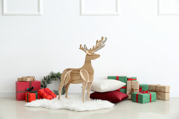 Wooden reindeer with Christmas presents, wreath and pillows near light wall