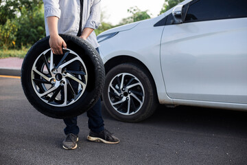 Rolls the tire. young man asia in aqua colored uniform works in the road. Close up view. Mechanic holding a tire at the repair garage. replacement of winter and summer tires.