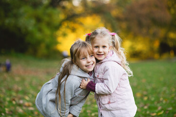 Fototapeta na wymiar Two child girls play on the lawn in the autumn park.