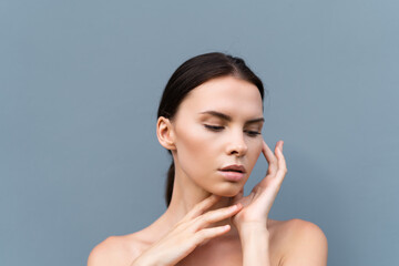 Close-up beauty portrait of a topless woman with perfect skin and natural make-up on light blue wall background