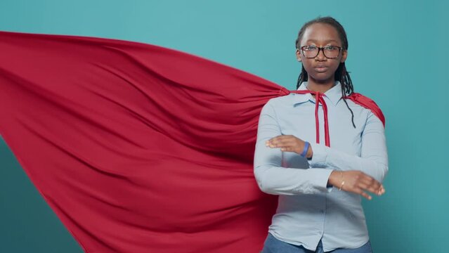 Portrait of female superhero wearing red cape costume from cartoon or comic book, showing strength and motivation. Woman posing as hero character with cloak, feeling confident.