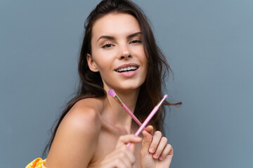 Close-up beauty portrait of woman with perfect skin and natural makeup, full nude lips, holding a bright pink eyeshadow brush, cosmetic concept