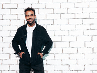 Handsome hipster model. Sexy unshaven man dressed in black  summer shirt and jeans clothes. Fashion male posing near white brick wall in studio at sunny day. Isolated