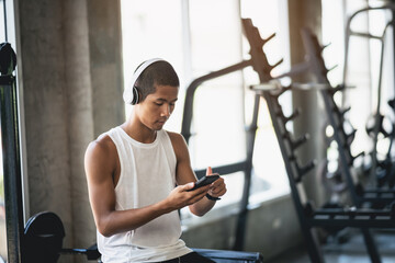 Asian man sportsman fit body wearing white headphone and using mobile phone to listen music while...
