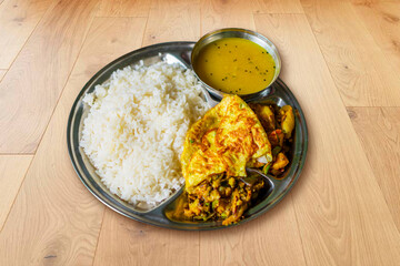 Steamed rice lentil dal mix vegetables Indian curry and an omelet on a lunch plate Bengali lunch dish
