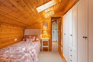 Narrow bedroom with beds and white wardrobe in a modern cottage with wooden walls.