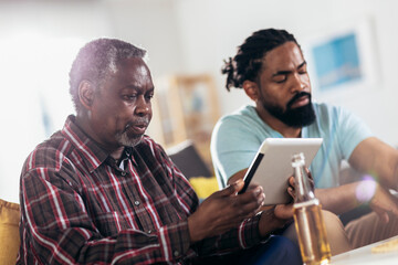 Smiling father and son using digital tablet in living room at home