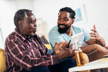 Smiling father and son using digital tablet in living room at home