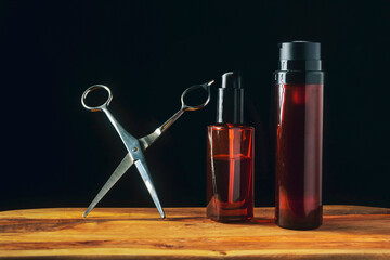 Obraz na płótnie Canvas Two brown oil bottles and metal scissors. Man grooming accessories on a wooden board, dark background. Hair and beard styling. Still life. Copy space
