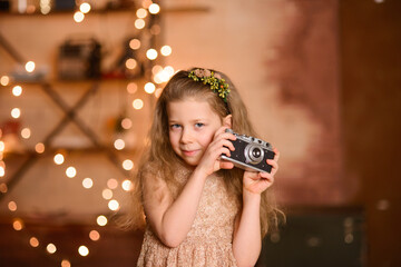 girl in a festive dress with flowing hair holds a vintage camera in her hands, New Year's garland lamps give yellow bokeh