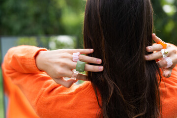 Pretty stylish woman in orange sweater posing with mirror outdoor, wearing colorful rings accessories on fingers, cute jewelry